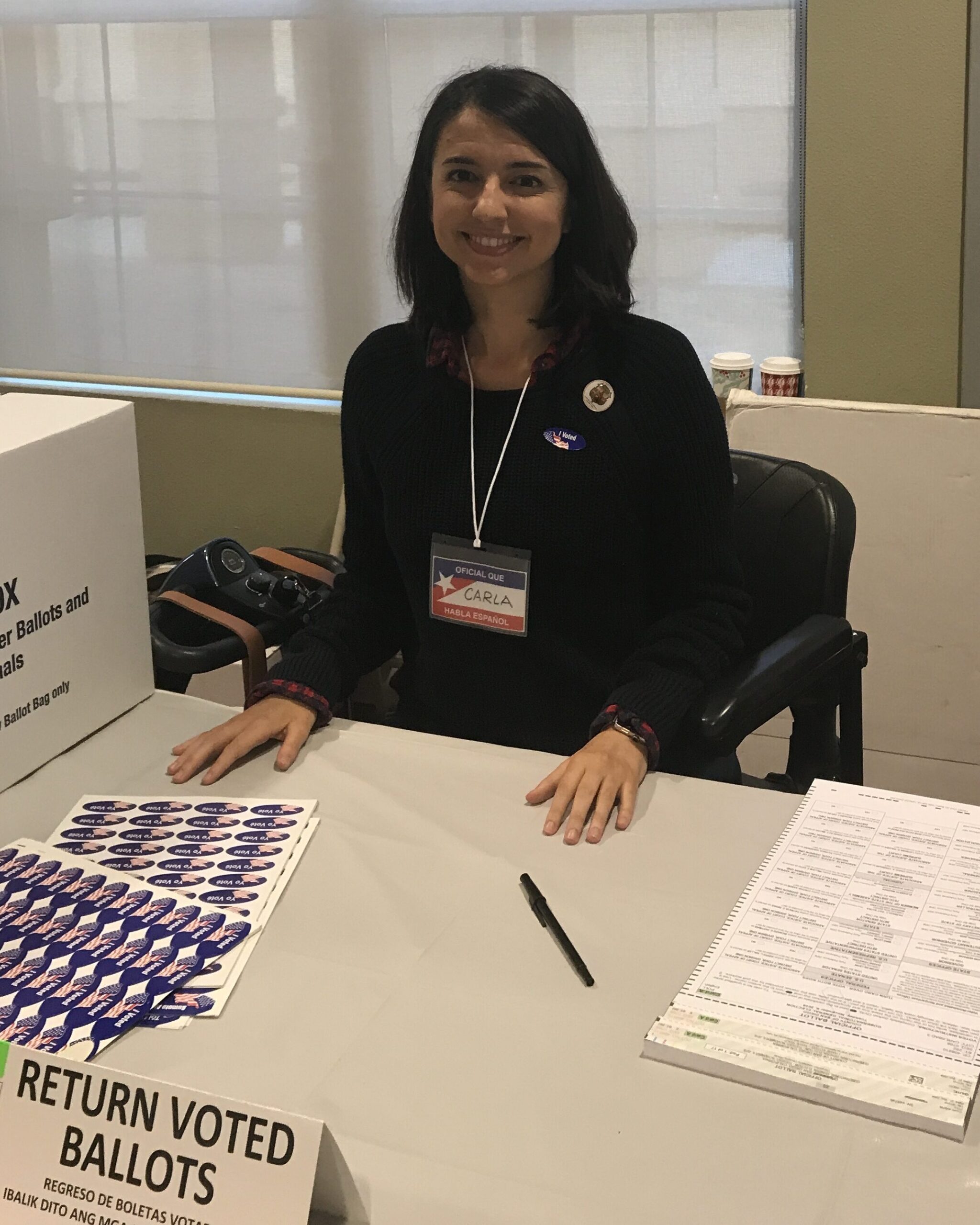 Photo of a volunteer named Carla S. from California sitting at a table working as a poll worker